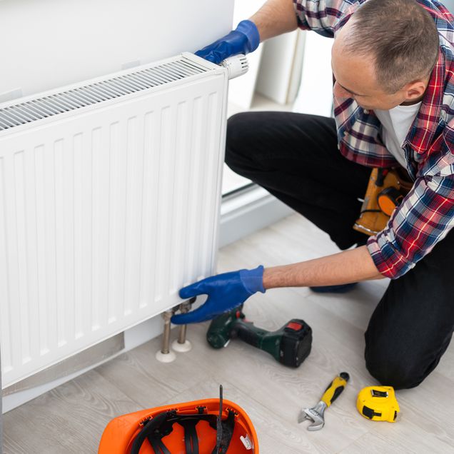 Handwerker montiert einen Flachheizkörper an die Wand.
