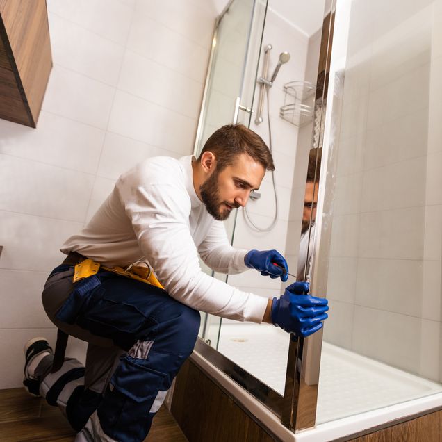 Handwerker baut eine Duschabtrennung ein.