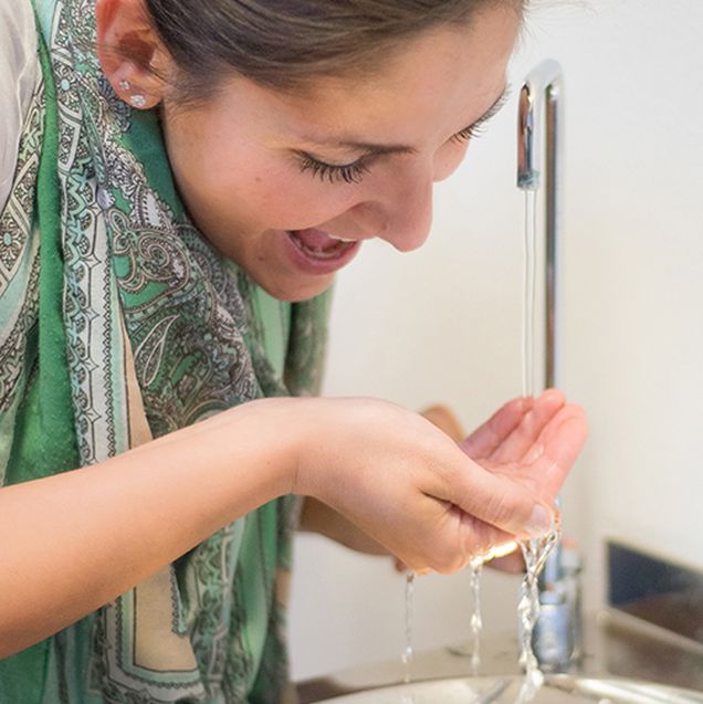 eine Frau hält ihre Hand unter den laufenden Wasserhahn