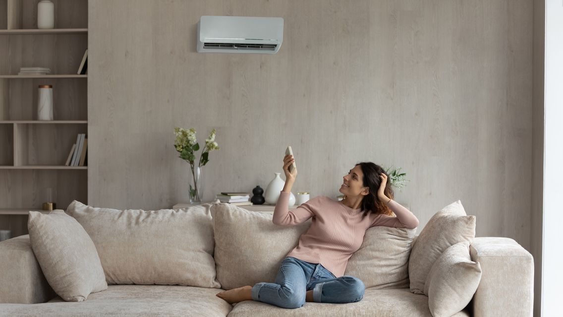 Junge Frau reguliert von der Couch aus die Klimaanlage.