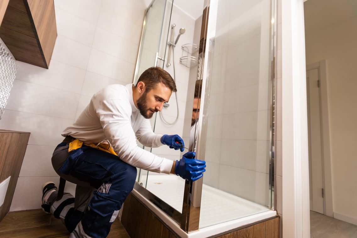 Handwerker baut eine Duschabtrennung ein.