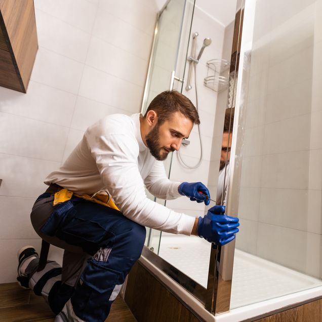 Handwerker baut eine Duschabtrennung ein.